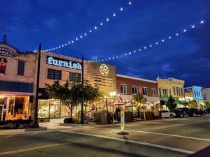 Downtown street at dusk with string lights and local shops.