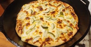 Homemade cheese pizza with pickles in cast iron skillet.