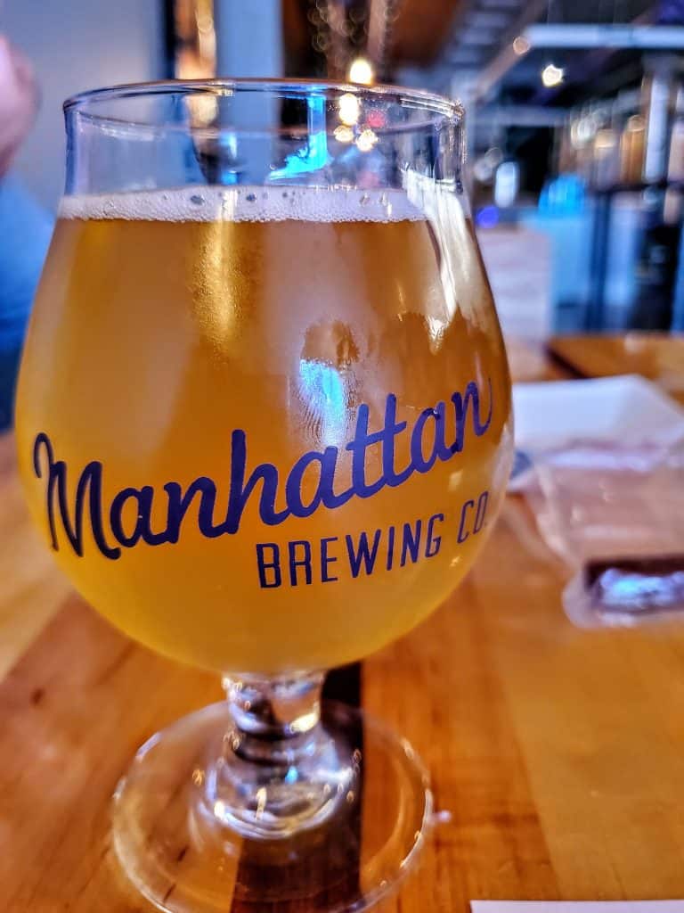 A glass of manhattan brewing company beer on a wooden table.