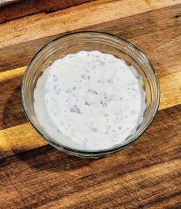 A bowl of dressing sitting on top of a cutting board.