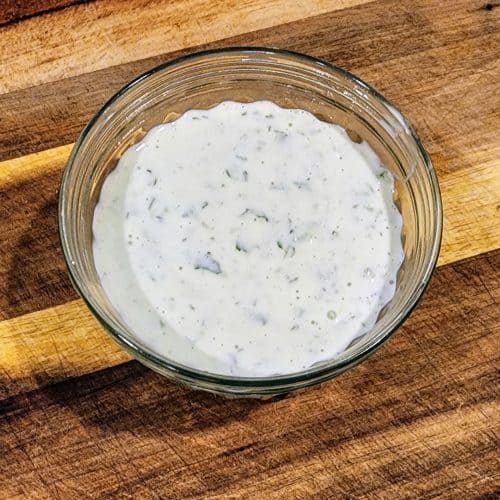 A bowl of dressing sitting on top of a cutting board.
