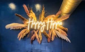 A neon sign that says happy hops on a blue wall.