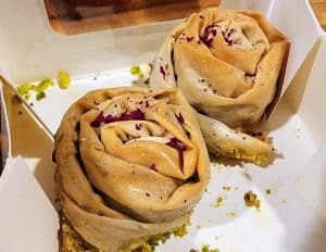 Two pastries with roses and pistachios in a box.