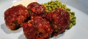 A plate with meatballs and peas on it.