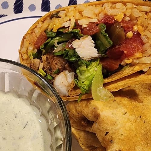 A plate with a burrito and a bowl of salsa.