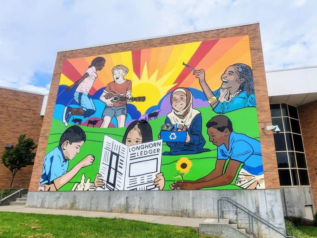 A mural depicting children reading in front of a building.