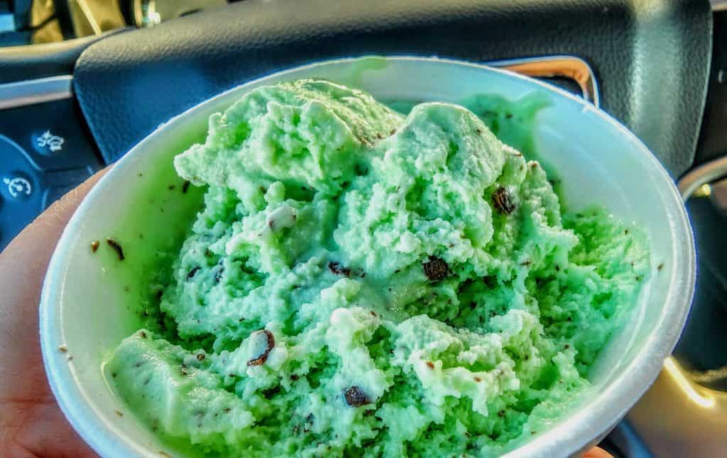 A person holding a bowl of green ice cream in a car.