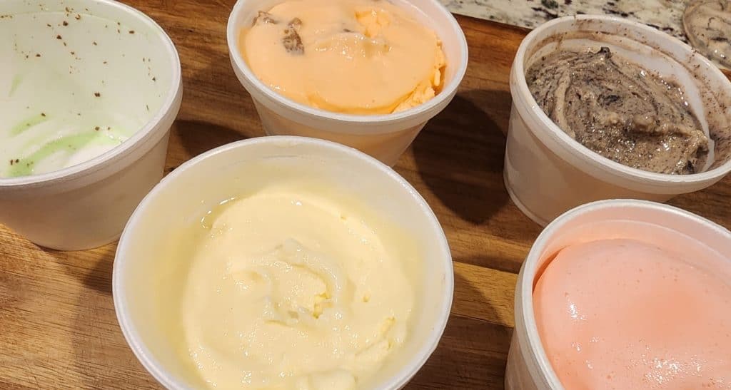 Five different kinds of ice cream in cups on a table.
