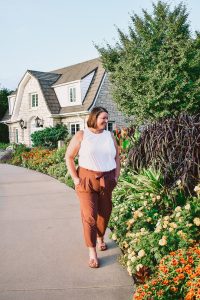 A woman wearing a white top and brown pants walking down a path.