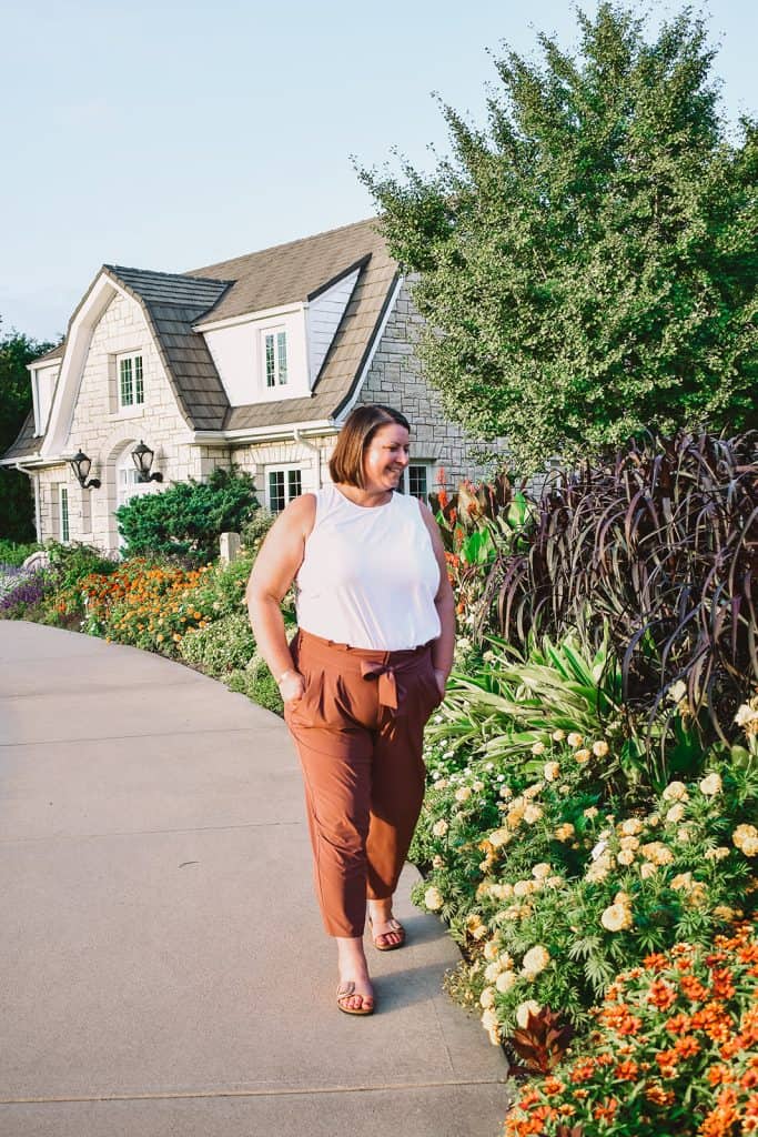 A woman wearing a white top and brown pants walking down a path.