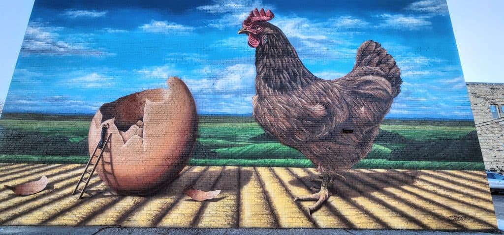 Mural of chicken and broken egg on building.