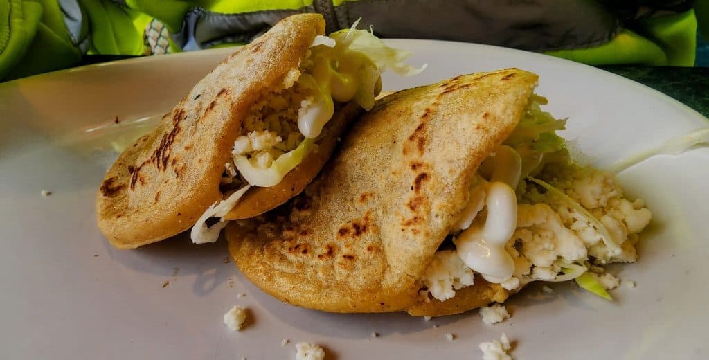 Two tacos from Frida's restaurant are sitting on a white plate.