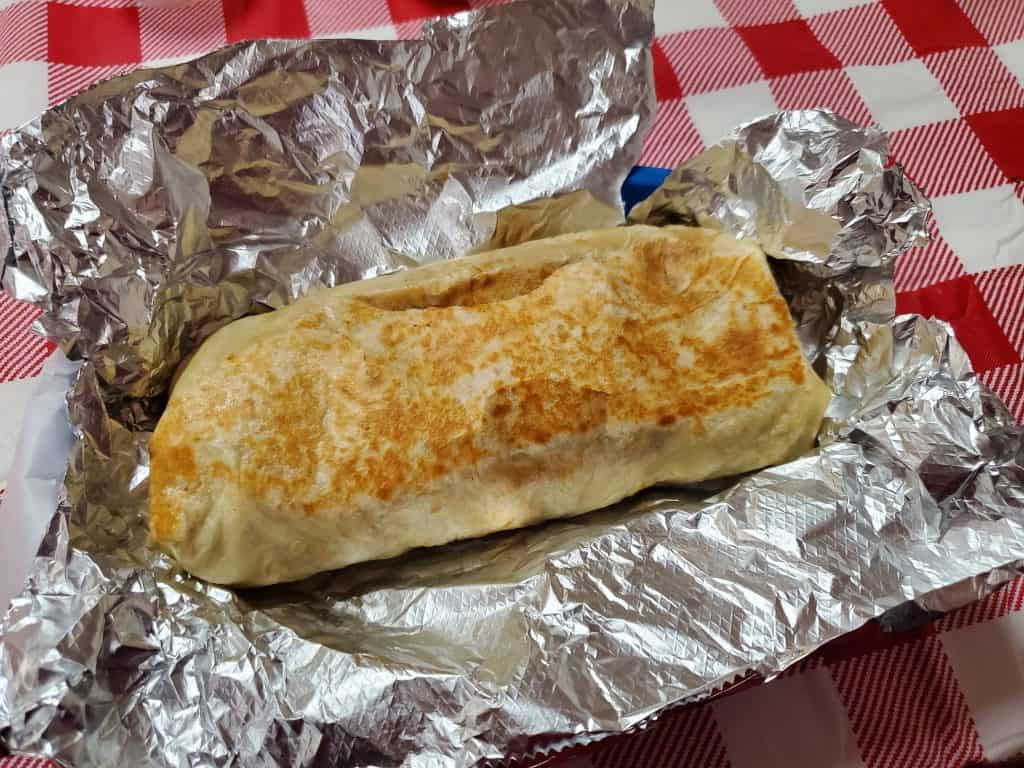 A burrito wrapped in foil on a red and white checkered tablecloth at Taqueria El Aguila in Manhattan, KS.