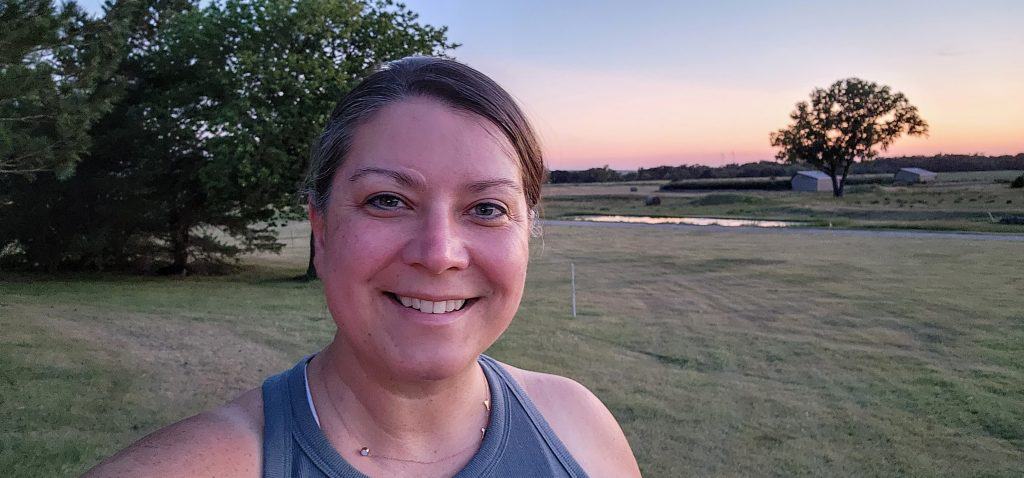 A person telling people they have cancer, smiling for a selfie with a sunset and an open field in the background.