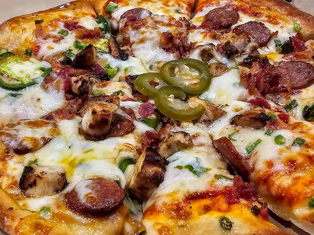 A mouth-watering pizza topped with melted cheese, pepperoni, ham, jalapeños, and green bell peppers from Highwind Brewing Company in Junction City KS, shown up close in its box.