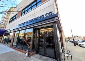 Exterior view of Highwind Brewing Company, a local brewery with a storefront featuring large windows, located on a sunny street corner in Junction City KS.
