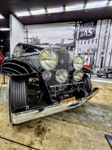 A black car with lights on is on display at the Car Museum in Manhattan, KS.