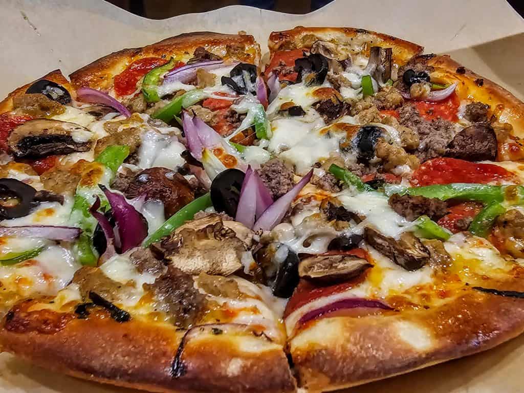 A freshly-baked pizza topped with melted cheese, pepperoni, mushrooms, black olives, green peppers, onions, and sausage from Highwind Brewing Company in Junction City KS, with a few slices