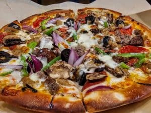 A freshly-baked pizza topped with melted cheese, pepperoni, mushrooms, black olives, green peppers, onions, and sausage from Highwind Brewing Company in Junction City KS, with a few slices