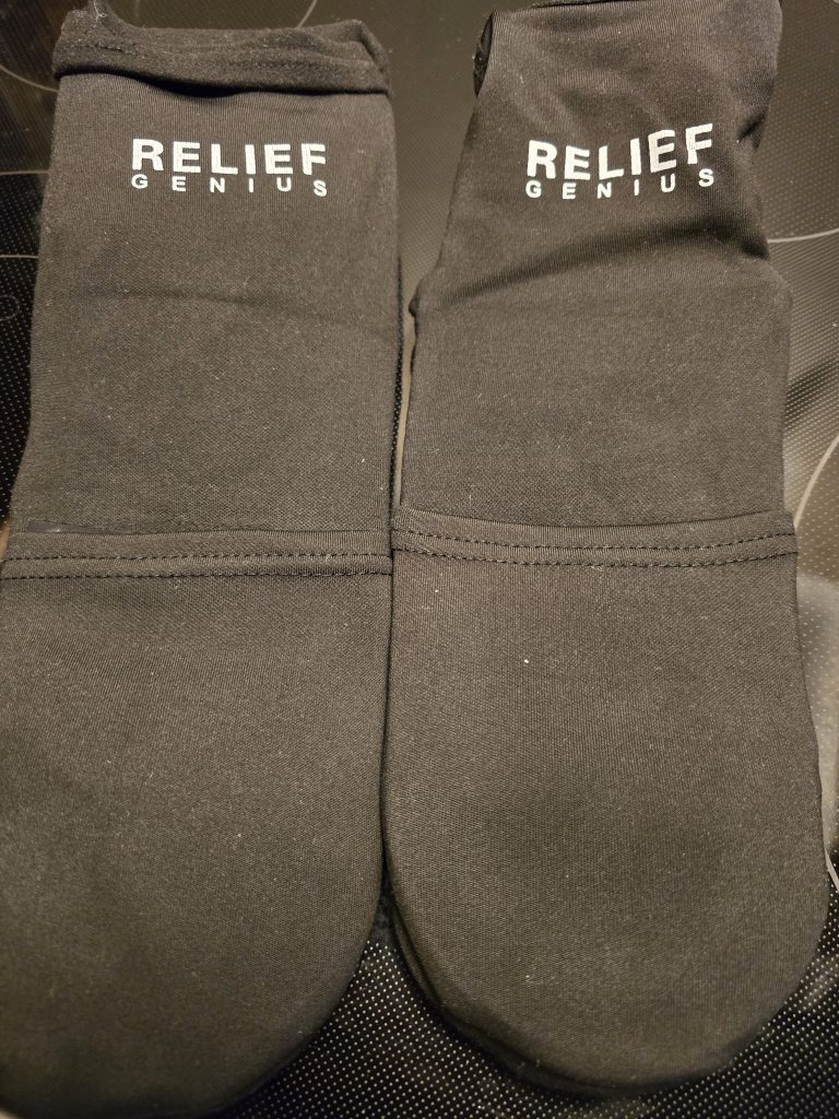 A pair of black socks with the words "RELIEF GENIUS" printed in white on the top, making things easier for those undergoing chemo. The socks are placed side by side on a dark surface.