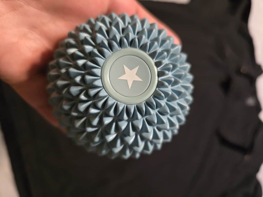 A hand holding a round, blue spiky massage ball with a white star in the center. The background is out of focus, showing a piece of dark clothing. Chemo patients may find it easier to manage stress with such helpful tips.