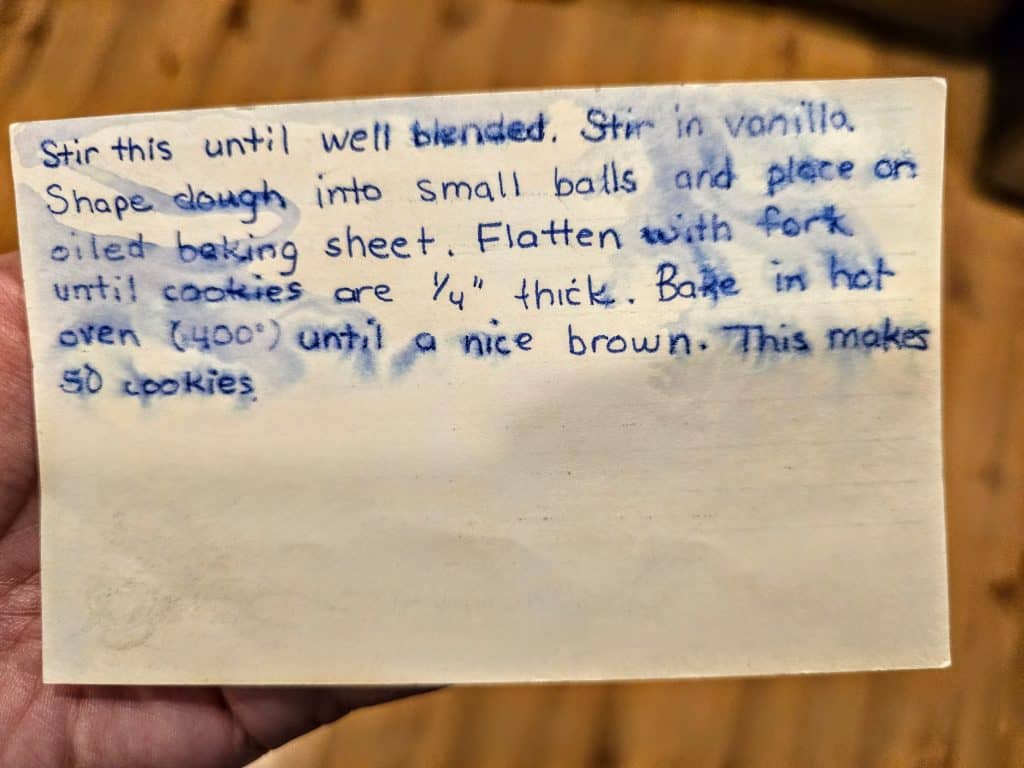A handwritten recipe card instructs to stir the mixture until well blended, add vanilla, shape dough into small balls, place on an oiled baking sheet, flatten with a fork until 1/4 inch thick, and bake at 400°F until brown. The recipe makes 50 cookies.