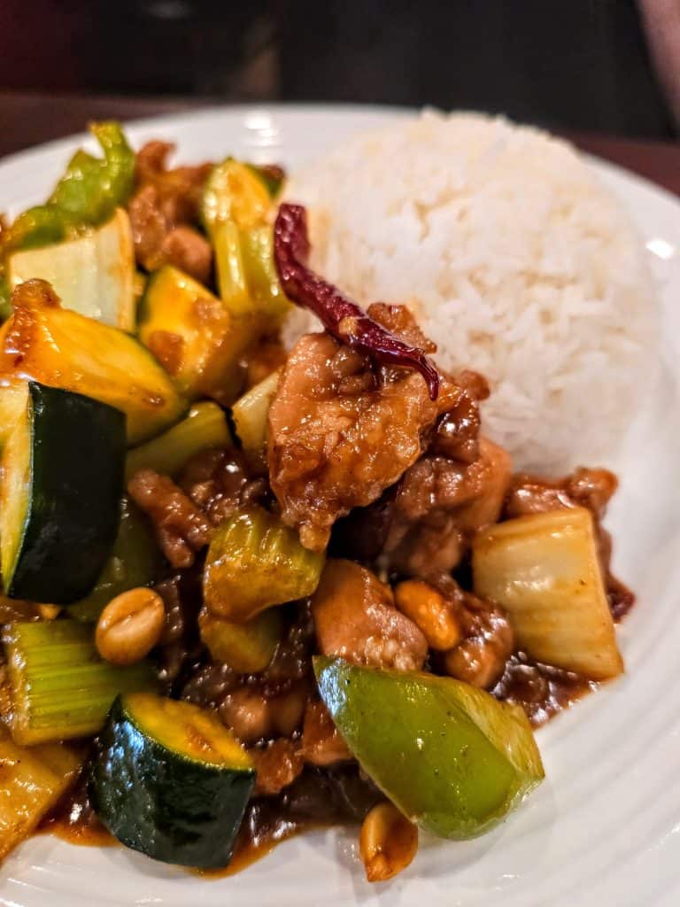 At Melanie's Kitchen in Hays, KS, enjoy a plate of stir-fried chicken with zucchinis, celery, and peanuts, coated in a savory sauce with a hint of dried chili pepper. It's served alongside a mound of fluffy white rice for the perfect meal.