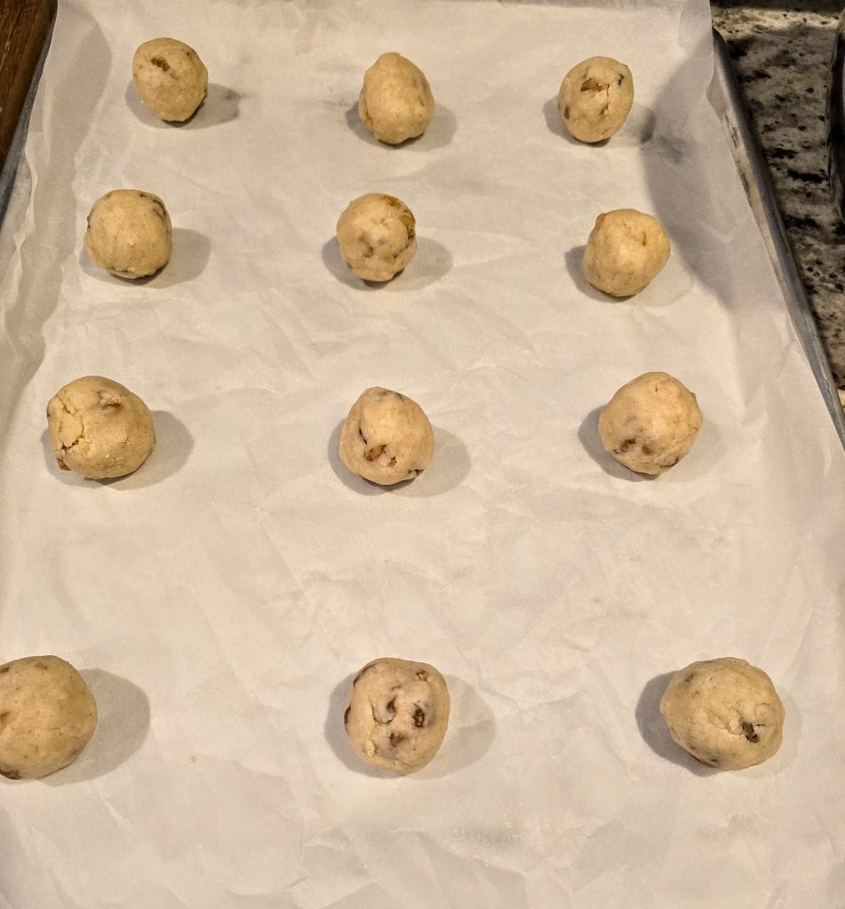 Twelve of Grandma Eva's Sandies cookie dough balls are evenly spaced on a parchment-lined baking sheet, ready for baking.