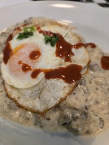 A fried egg topped with cilantro rests on a plate of creamy mushroom sauce in a cozy caf&eacute; in Manhattan, KS. Drops of hot sauce are drizzled on top, adding a splash of color and bringing the dish full circle.