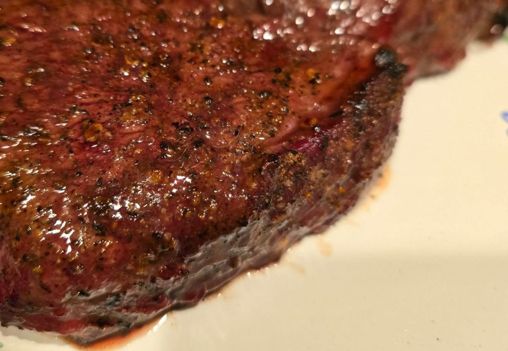 Close-up of two seared beef steaks on a white plate with a blue zigzag pattern. The steaks have a rich, brown crust with visible seasonings and juices glistening on the surface. Perfect for those in Manhattan, KS craving savory perfection.
