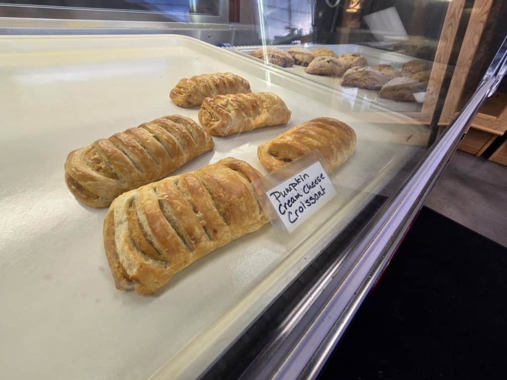 The KS Bakery in Hays showcases pumpkin cream cheese croissants with golden, flaky crusts. A label identifies them in the foreground, with other tempting pastry options visible in the background.