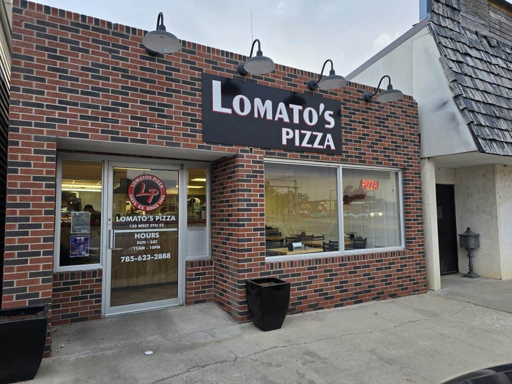 Brick facade of Lomato's Pizza. A large sign on the window features their logo, address, and phone number. The entrance boasts glass doors adorned with a pizza graphic, while three decorative lamps hang gracefully above the sign.