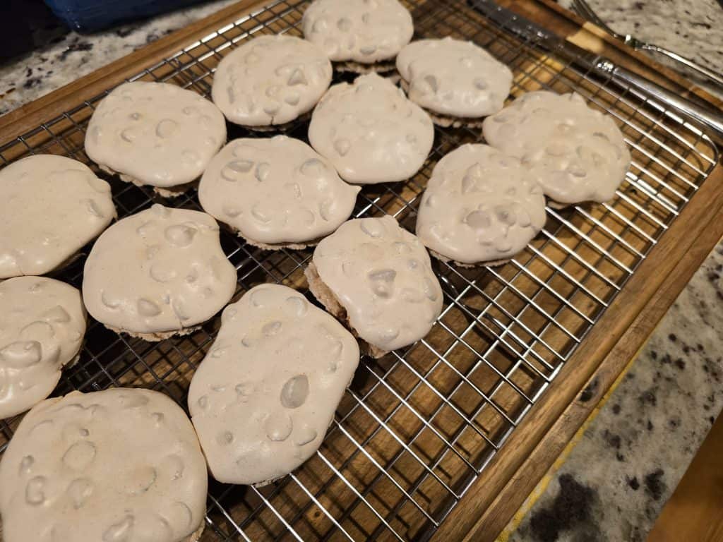 A batch of Grandma's freshly baked meringue cookies, known as Forgotten Cookies, boasts a slightly golden hue and tiny air bubbles on the surface. They are cooling on a metal rack placed over a granite countertop.