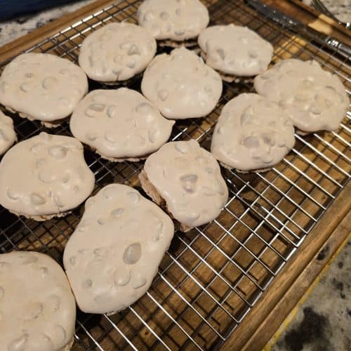A batch of Grandma's freshly baked meringue cookies, known as Forgotten Cookies, boasts a slightly golden hue and tiny air bubbles on the surface. They are cooling on a metal rack placed over a granite countertop.