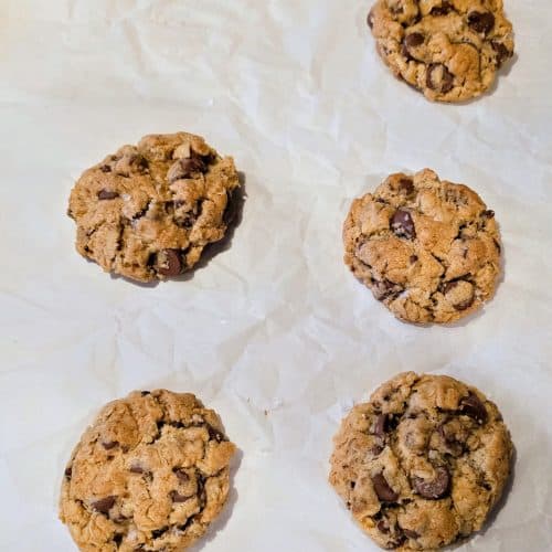 Ten of Grandma's chocolate chip cookies are arranged on white parchment paper. These treats are golden brown with visible chocolate chunks, suggesting a freshly baked texture that takes you back to comforting afternoons in her cozy kitchen.