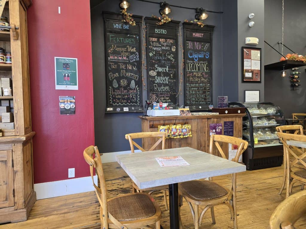Nestled in Hays, KS, the cozy cafe interior of Paisley Pear boasts chalkboard menus on vibrant red walls. Wooden furniture surrounds a small table beside a glass display case filled with pastries, while tasteful decorations add to the warm and inviting atmosphere.