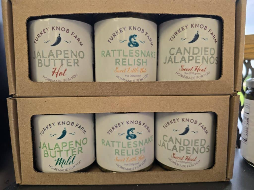Six jars of Turkey Knob Farm goodies in cardboard packaging: hot and mild jalapeno butter, rattlesnake relish with a "sweet little bite," and candied jalapenos labeled "sweet heat." Available locally at Simon Meat Locker in Olsburg KS.