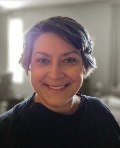 A person with short, dark hair smiles at the camera in a softly lit room with neutral-colored walls&mdash;capturing a moment of warmth and optimism during cancer recovery.
