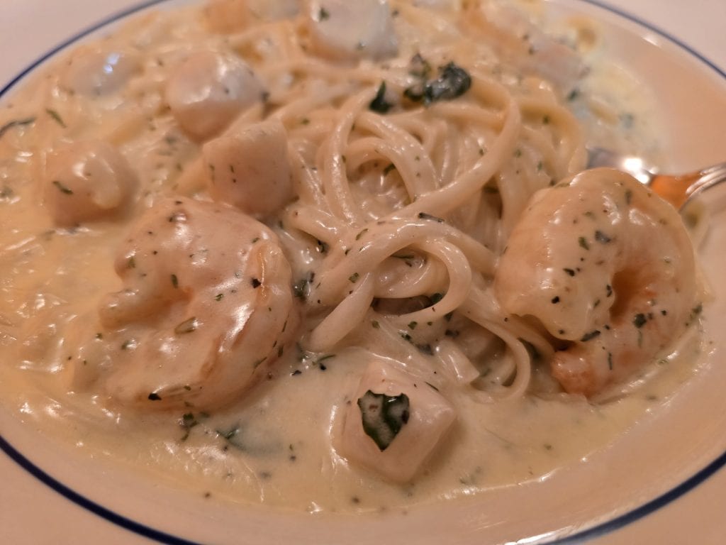 A close-up of creamy seafood pasta with shrimp, scallops, and spaghetti noodles in a rich white sauce, served at an Italian restaurant in Hays KS on a white plate with a blue rim.