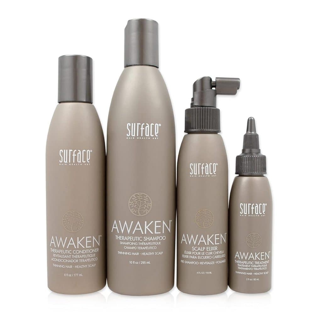 Four bottles of Surface Awaken hair regrowth products in matte taupe packaging—including therapeutic conditioner, shampoo, scalp elixir spray, and a dropper bottle—arranged upright against a white background, ideal for supporting hair growth after chemo.