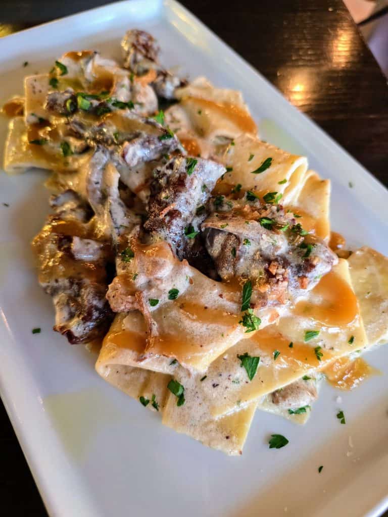 Wide pasta ribbons topped with a creamy mushroom sauce and chopped parsley, perfect for Manhattan KS food lovers seeking a cozy breakfast or memorable date nights, served on a rectangular white plate.
