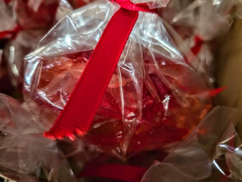 A close-up of a clear plastic bag containing Linda's Hard Candy, tied with a bright red ribbon. The bag and ribbon are in sharp focus, with a soft, blurred background.