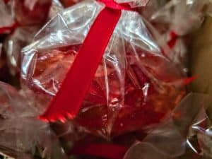 A close-up of a clear plastic bag containing Linda's Hard Candy, tied with a bright red ribbon. The bag and ribbon are in sharp focus, with a soft, blurred background.