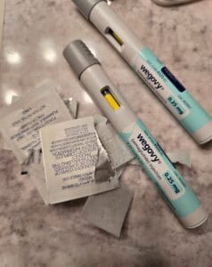Two Wegovy injection pens labeled 0.25 mg sit on a marble surface with opened alcohol prep pads and discarded wrappers nearby. These GLP-1 pens are designed for subcutaneous injection, supporting your personal decision in managing health.