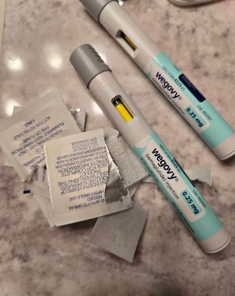 Two Wegovy injection pens labeled 0.25 mg sit on a marble surface with opened alcohol prep pads and discarded wrappers nearby. These GLP-1 pens are designed for subcutaneous injection, supporting your personal decision in managing health.