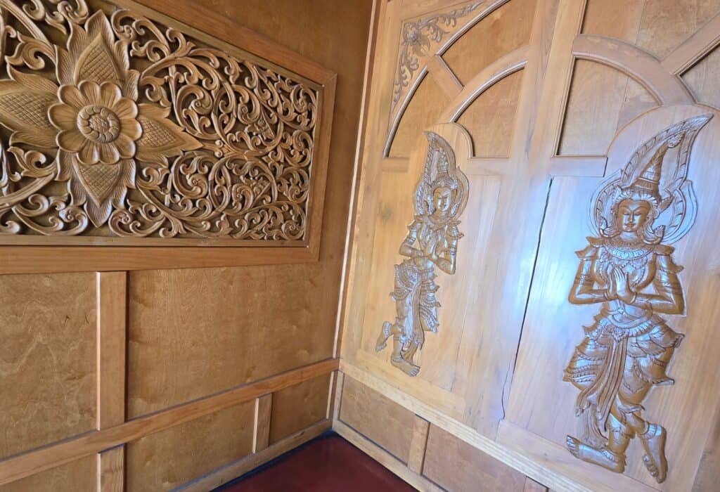 Intricately carved wooden wall art featuring ornate floral patterns and two detailed figures of traditional dancers on a wooden door, reminiscent of the décor at Baan Thai, one of Manhattan Kansas' beloved restaurants.