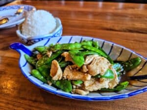 A bowl of stir-fried chicken with snap peas in sauce is served in a blue and white dish, with a side of steamed white rice&mdash;just one of the flavorful offerings at Baan Thai, one of the beloved restaurants among Manhattan Kansas restaurants.